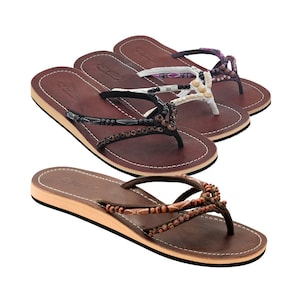 Könnte beinhalten: Drei Paar braune Ledersandalen mit Perlenriemen. Die Sandalen haben einen einfachen Zehentrenner-Stil und sind mit bunten Perlen verziert.