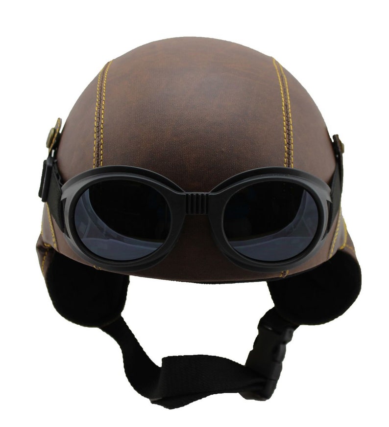 K&ouml;nnte beinhalten: Brauner Helm in Lederoptik mit schwarzer Brille. Der Helm hat gelbe N&auml;hte und Ohrenklappen. Die Brille hat dunkle Gl&auml;ser und einen schwarzen Riemen. Motorrad- oder Fliegerhelm im Vintage-Stil.