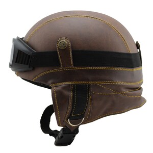 K&ouml;nnte beinhalten: Brauner Motorradhelm aus Leder mit gelben N&auml;hten und schwarzer Brille. Der Helm hat ein Vintage-Design mit schwarzem Riemen und Schnalle. Die Brille ist schwarz und mit einem schwarzen Gummiband befestigt.