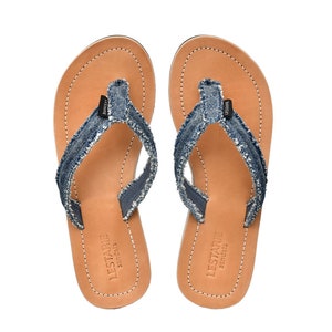 May include: A pair of brown leather sandals with blue denim straps and frayed edges. The sandals have a simple design and are perfect for casual wear.