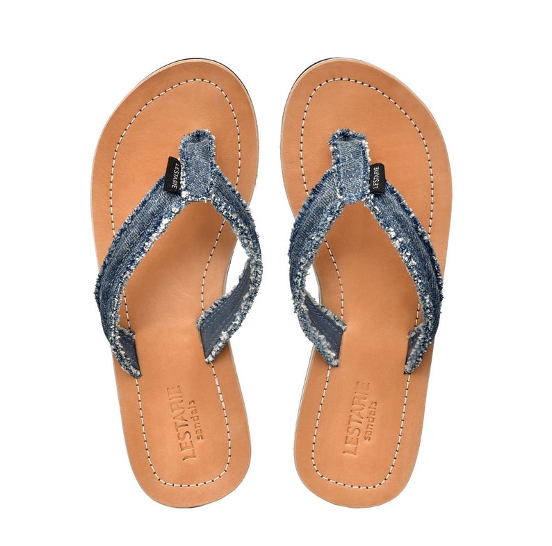 May include: A pair of brown leather sandals with blue denim straps and frayed edges. The sandals have a simple design and are perfect for casual wear.