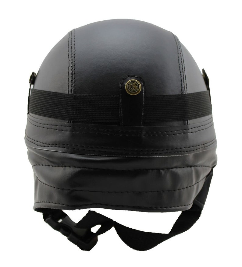 K&ouml;nnte beinhalten: Schwarzer Motorradhelm aus Leder mit Steppn&auml;hten. Er hat ein schwarzes Gummiband und einen Schnallenriemen zur Befestigung. Enth&auml;lt einen dekorativen Messingknopf auf der R&uuml;ckseite.