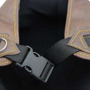 K&ouml;nnte beinhalten: Nahaufnahme eines braunen Motorradhelms aus Leder mit gelben N&auml;hten. Der Helm hat einen schwarzen Riemen mit einer Kunststoffschnalle und einen silbernen Metallring. Das Innere des Helms ist schwarz.