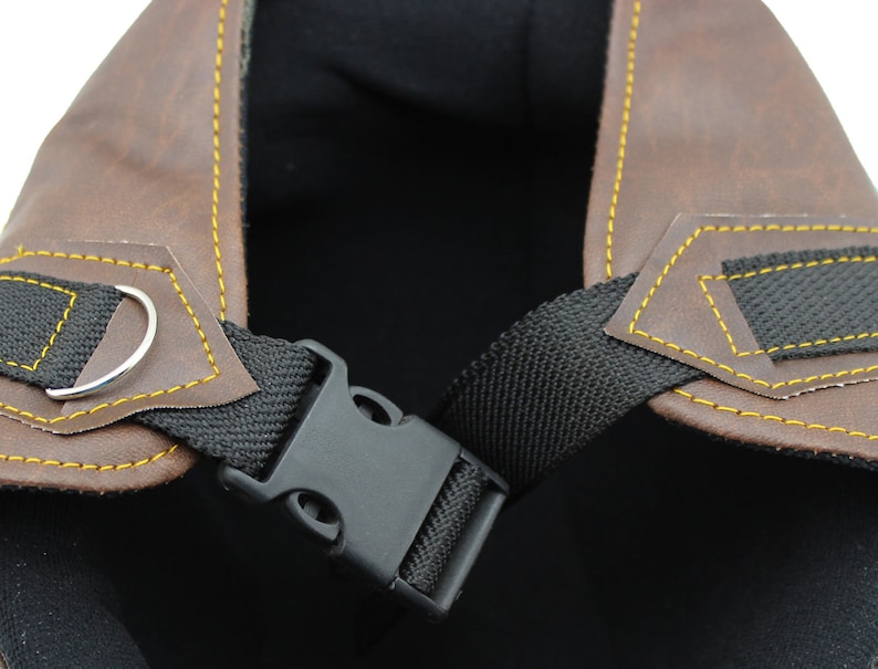 K&ouml;nnte beinhalten: Nahaufnahme eines braunen Motorradhelms aus Leder mit gelben N&auml;hten. Der Helm hat einen schwarzen Riemen mit einer Kunststoffschnalle und einen silbernen Metallring. Das Innere des Helms ist schwarz.