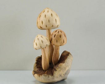 May include: A wooden mushroom sculpture featuring three mushrooms with carved details. The caps have small, evenly spaced holes. The mushrooms are light brown and beige, and are attached to a textured base.