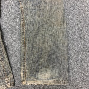 May include: Close-up of faded blue denim jeans. The jeans show wear and tear, with a distressed look. The hem is frayed, and the fabric has a textured appearance. The jeans are likely vintage or have a worn-in style.