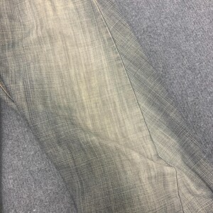 May include: Close-up of denim pants in shades of gray and beige. The fabric has a textured appearance with visible vertical and horizontal threads. The pants are folded, showing a seam and a portion of the leg.