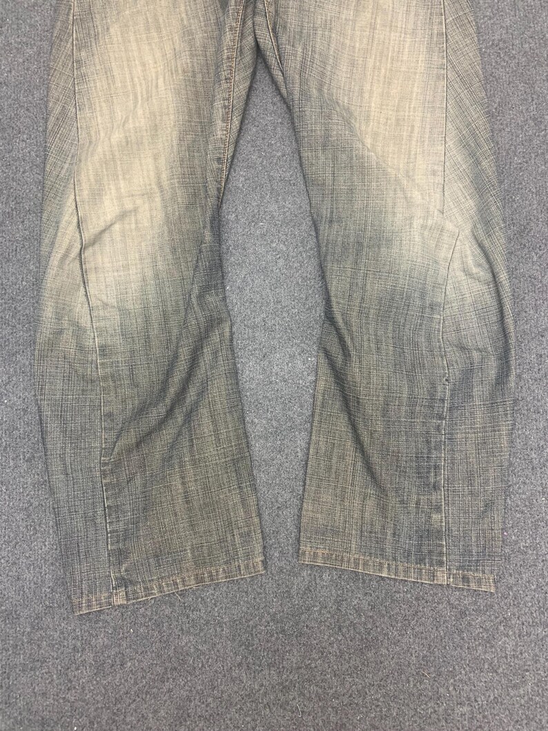 May include: Faded denim jeans with a straight leg cut. The jeans have a worn, distressed appearance with lighter areas on the thighs and knees. The fabric has a textured look.