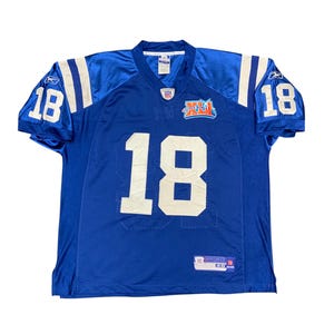 Könnte beinhalten: Ein blaues Football-Trikot mit der Nummer 18 in Weiß auf der Vorderseite, dem Rücken und den Ärmeln. Das Trikot hat weiße Streifen auf den Schultern und einen Super Bowl XLII-Patch. Das Trikot besteht aus atmungsaktivem Mesh-Material.