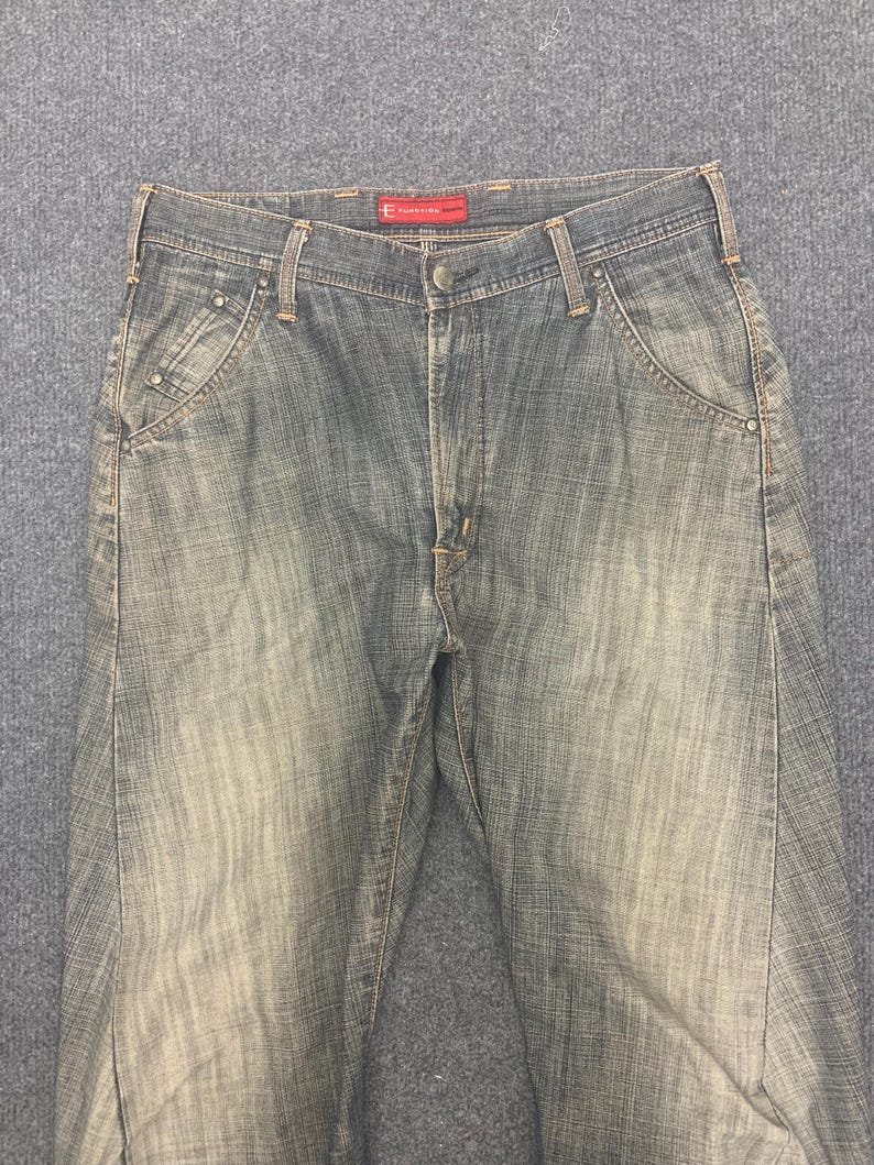 May include: Faded blue denim jeans with a classic five-pocket design. The jeans have a button and zipper closure, belt loops, and a subtle faded wash effect. The brand label is visible on the waistband.