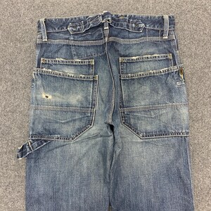 Puede incluir: Vaqueros de mezclilla azul con un aspecto desgastado, con m&uacute;ltiples bolsillos y un dise&ntilde;o de estilo carpintero. Los vaqueros tienen un lavado descolorido y detalles de costura visibles, con cierre de bot&oacute;n y cremallera.