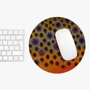 May include: Round mousepad featuring a brown trout skin pattern with black, blue, and red spots. A white computer mouse rests on the mousepad, next to a white keyboard.