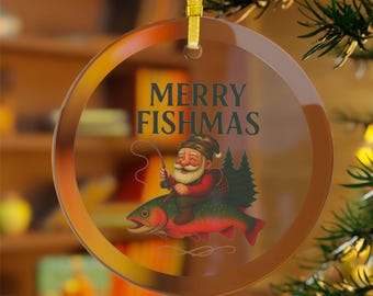 May include: A round, clear glass Christmas ornament with a gold ribbon. The ornament features the text "MERRY FISHMAS" above a cartoon of a gnome fishing on a red fish. The gnome wears a red coat and a green hat.