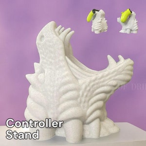 May include: White 3D printed controller stand shaped like a dragon's head with an open mouth. The stand is on a white surface. The text "Controller Stand" is visible below the stand.