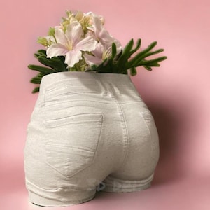 May include: White ceramic planter shaped like a pair of denim shorts with a bouquet of pink flowers.