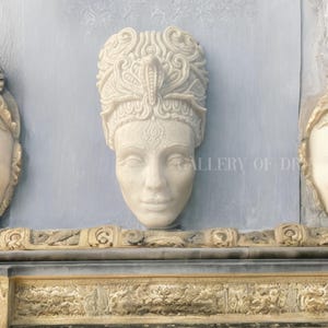 May include: A carved stone bust of a woman with an ornate headdress featuring a cobra. The bust is mounted on a light blue wall with a decorative border below. The text "GALLERY OF DREAMS" is visible.