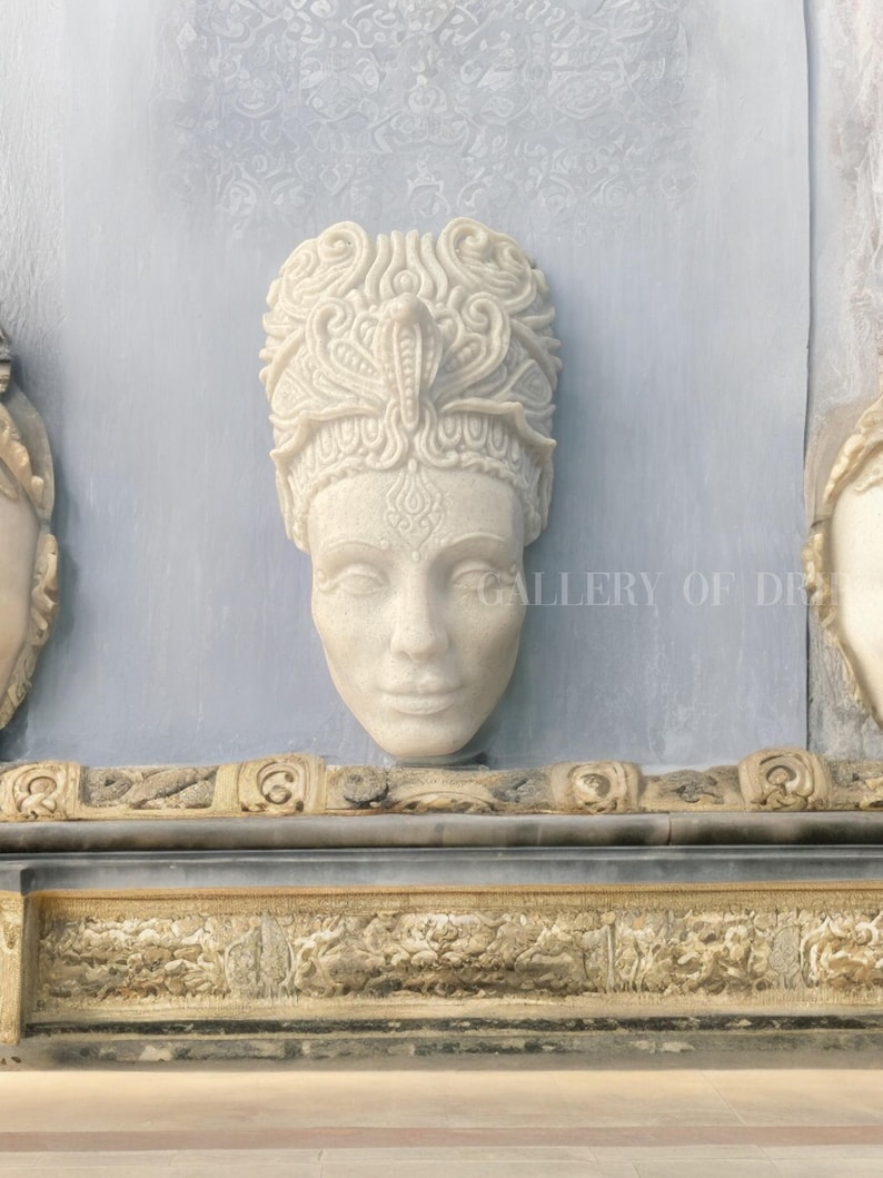 May include: A carved stone bust of a woman with an ornate headdress featuring a cobra. The bust is mounted on a light blue wall with a decorative border below. The text "GALLERY OF DREAMS" is visible.