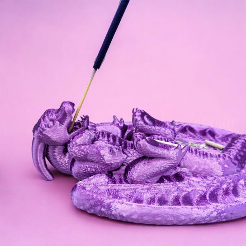 May include: Purple dragon incense burner with a blue incense stick burning. The dragon is curled up with its head raised and its tail curled around its body.