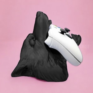 May include: A black 3D printed animal figure holding a white video game controller. The figure is standing on a pink surface.