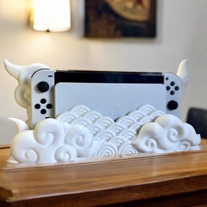 May include: White Nintendo Switch console with white Joy-Cons, sitting in a white 3D printed stand with a cloud and wave design.