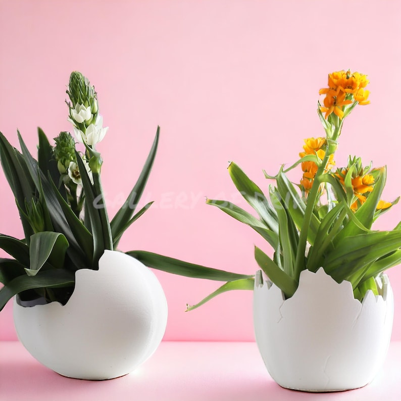 May include: Two white ceramic egg-shaped planters with cracked edges, one with a white flower and green leaves, the other with yellow flowers and green leaves.