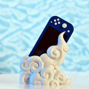 May include: A white cloud-shaped stand with a blue Nintendo Switch Lite console resting inside. The stand is designed with swirling cloud patterns.
