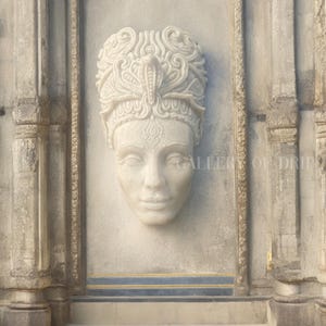 May include: A white marble sculpture of a woman's face with ornate headwear, including a cobra. The sculpture is set into a stone wall with decorative columns and trim. The text "GALLERY OF DRIP" is visible in the upper right corner.