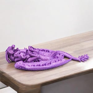 May include: A purple 3D printed dragon figurine with intricate details. The dragon is curled up with its wings spread out.