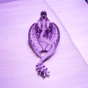 May include: A purple dragon figurine with wings outstretched and a curled tail. The dragon is made of a textured material and has a detailed design.