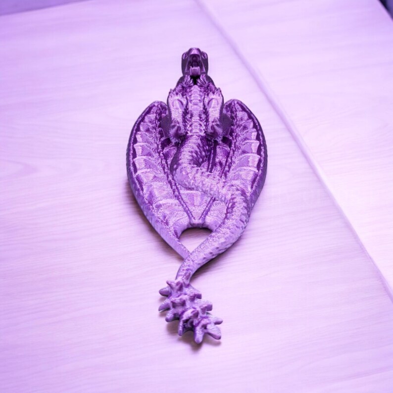 May include: A purple dragon figurine with wings outstretched and a curled tail. The dragon is made of a textured material and has a detailed design.