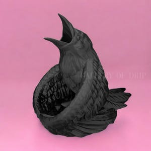 May include: A black raven sculpture with its beak open wide, as if it is singing. The raven is perched on a nest made of its own feathers. The sculpture is made of a smooth, matte black material.