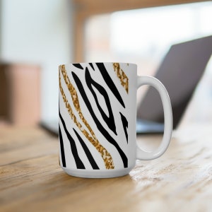 Könnte beinhalten: Weiße Keramiktasse mit einem Zebra-Muster in Schwarz und Gold.