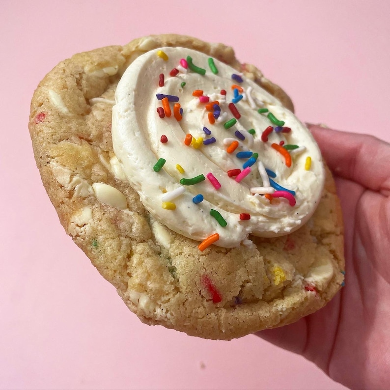 K&ouml;nnte beinhalten: Nahaufnahme eines Schokoladen-Chip-Kekses, der mit Vanille-Frosting und bunten Streuseln verziert ist.