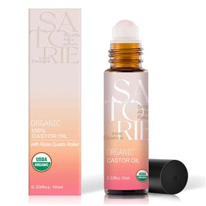 May include: A bottle of organic castor oil with a rose quartz roller, next to a matching box. The bottle and box have a gradient pink and white background with the text "SATORIE Inner Essence" and "Organic Castor Oil". The bottle is 0.33 fl oz, 10 ml.