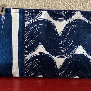 May include: A blue and white zippered pouch with a wavy pattern. The pouch is made of fabric and has a zipper closure.
