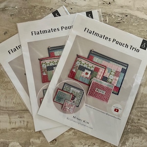 May include: Several sewing pattern packets titled "Flatmates Pouch Trio" and "Flatmates Pour" are displayed. The packets feature images of colorful, quilted pouches. The packets are in clear plastic sleeves, with the designer's name and website address visible.