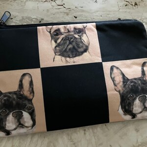 May include: Black and tan zippered pouch with a checkerboard pattern. The squares feature detailed illustrations of French Bulldogs. The pouch has a black zipper and a small tag.