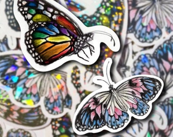 Puede incluir: Dos pegatinas de mariposas coloridas. La primera mariposa es una monarca con alas de arcoíris. La segunda mariposa tiene alas rosas, azules y blancas.
