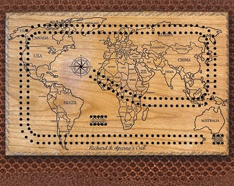 May include: A wooden world map cribbage board with black dots and a compass in the center. The board is engraved with the text "Richard & Aparna's Crib".