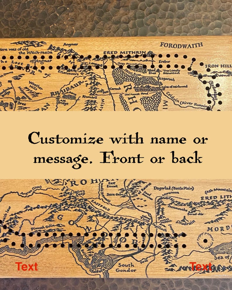 May include: Wooden cribbage board featuring a map design with black peg holes. The map includes text and geographical features. The board is customizable with a name or message on the front or back.