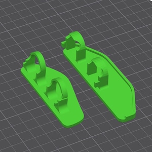 Puede incluir: Dos piezas de plástico verde impresas en 3D con múltiples agujeros y una forma curva. Las piezas están diseñadas para ser utilizadas como soporte para una impresora 3D.