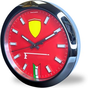 Pode incluir: Um relógio redondo com mostrador vermelho com um emblema de escudo amarelo e a letra "F". O relógio tem uma moldura preta e uma borda prateada brilhante. Os ponteiros são pretos e os marcadores de hora são retângulos brancos.