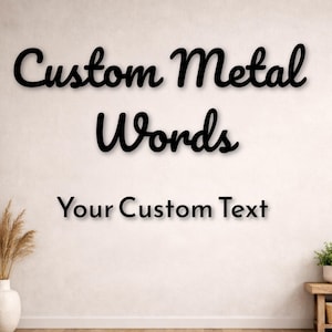 Può includere: Cartello in metallo nero con la scritta "Custom Metal Words" in corsivo e "Your Custom Text" in sans-serif. Il cartello è esposto su una parete bianca sopra un pavimento in legno.