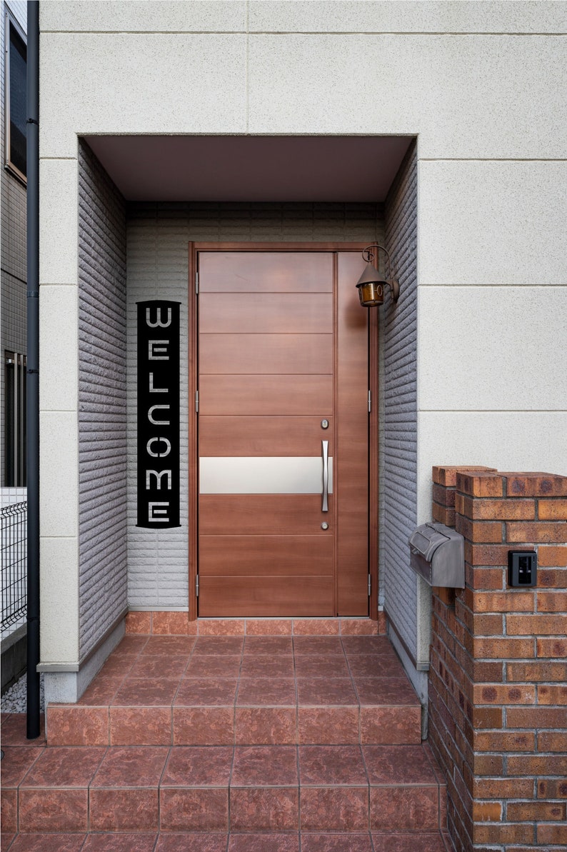 Pu&ograve; includere: Una porta d'ingresso in legno con un accento argentato orizzontale e un cartello nero con la scritta "WELCOME". La porta &egrave; inserita in un ingresso incassato con un esterno in mattoni e pietra. Una lanterna in stile vintage &egrave; montata sopra la porta.