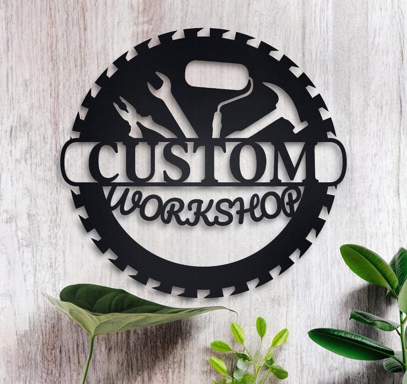 May include: Black metal sign with a saw blade design and the words "CUSTOM WORKSHOP" in a banner. The sign features a variety of tools, including a paint roller, a hammer, and a wrench.