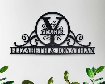 Peut inclure: Une plaque de maison personnalisée en métal noir avec un motif de volutes décoratives. La plaque porte le nom de famille "Yeager" et les prénoms "Elizabeth & Jonathan".