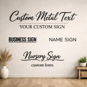 May include: Black metal signs on a white wall. The signs read "Custom Metal Text", "Your Custom Sign", "Business Sign", "Name Sign", "Nursery Sign", and "custom fonts". A vase with dried plants and a small table with a plant are in the image.