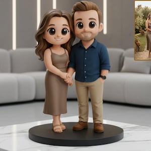 May include: A figurine of a couple holding hands, standing on a black circular base. The woman wears a brown dress and sandals, while the man wears a blue shirt, khaki pants, and brown shoes. A framed photo of the couple is in the background.