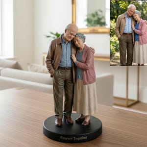 Könnte beinhalten: Eine Figur eines älteren Paares, das sich umarmt. Der Mann trägt eine braune Jacke, ein blaues Hemd und eine braune Hose. Die Frau trägt eine rosa Strickjacke, ein blaues Hemd und einen beigen Rock. Der Sockel ist schwarz und trägt die Aufschrift "Forever Together".