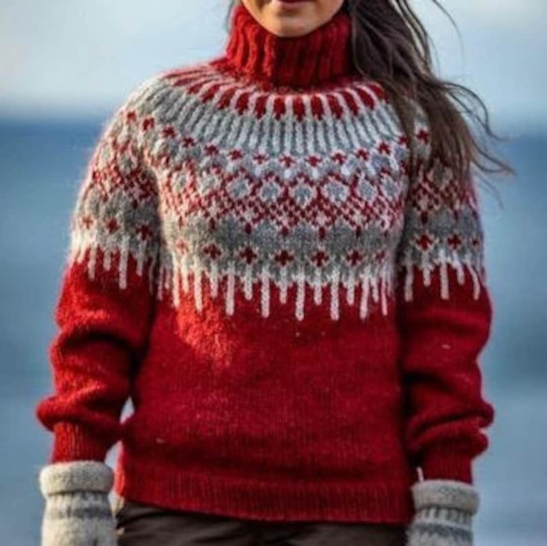 Puede incluir: Un su&eacute;ter de punto rojo, gris y blanco con un patr&oacute;n tradicional escandinavo. El su&eacute;ter tiene cuello alto y mangas largas.